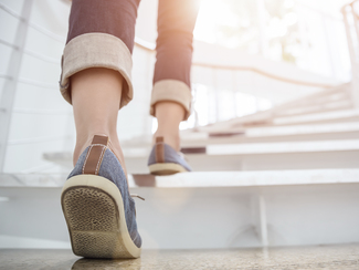 Eine Person geht die Treppe hinauf, man sieht nur die beiden Beine