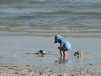 Ein Kind in UV-Schutzkleidung spielt am Strand