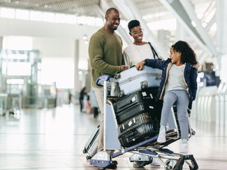 Ein Mann, eine Frau und ein Kind fahren mit einem Gepäcktrolley und Koffern durch einen Flughafen.