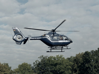 Ein Hubschrauber fliegt tief über ein Waldstück (Bild anzeigen)