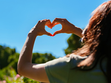 A woman forms a heart shape with her hands against the backdrop of a cloudless sky